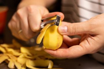 Close up of female hands peeling raw yellow potato, blurred background 