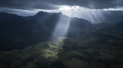 Dramatic aerial view of sun rays illuminating terraced rice fields nestled amidst majestic mountains.