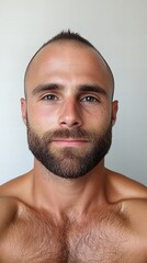 Fototapeta premium Close-up portrait of a young man with a mohawk hairstyle and full beard. He has a serious expression and a muscular physique.