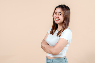 A confident young woman smiling with her arms crossed, showcasing a relaxed demeanor against a soft...