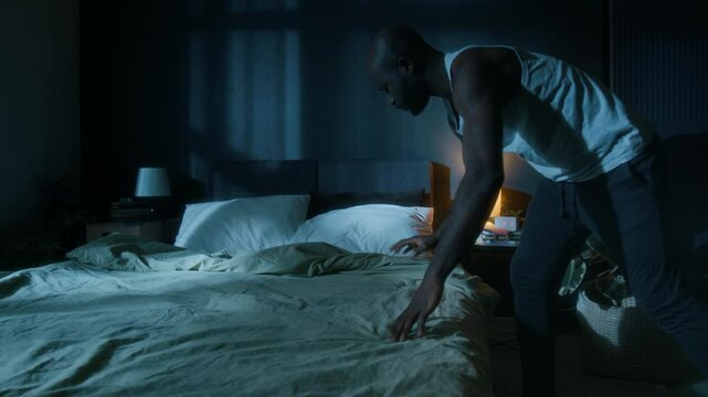 African American man praying before getting to bed and falling asleep on his back at night in modern dimly lit bedroom
