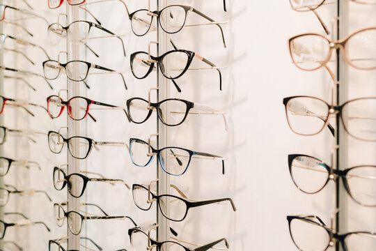 Customer chooses eyeglasses with clear lenses from the shelf. Eyesight correction. Stand of eyeglasses with different frames in the optical store.