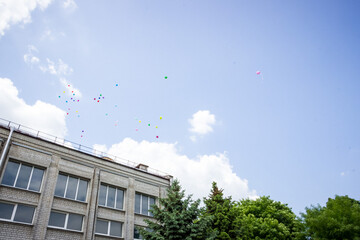 colorful balloons into the sky, flying, building, blue, white clouds, school yard, gymnasium, 