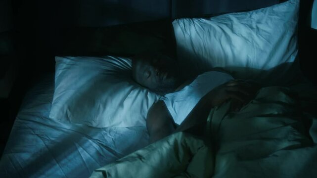 African American man tossing and turning, having nightmare, while sleeping in bed under warm blanket