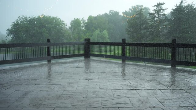 Rain falling on backyard with fancy wooden fence and green background, on a wet summer partly sunny day.