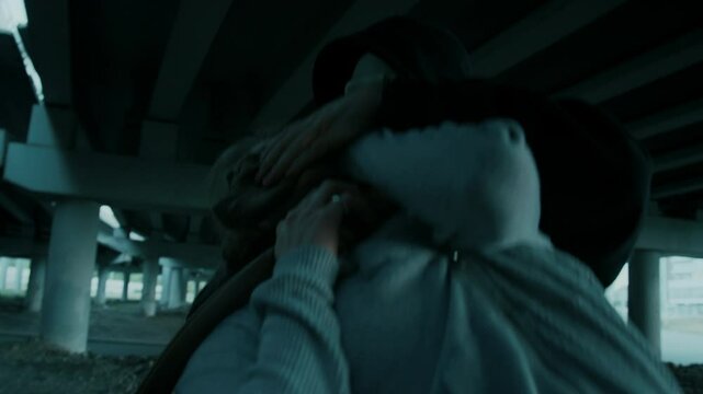 Handheld lowkey shot of masked male criminal clothing female victims mouth with chloroform-soaked rag under bridge on desolated street, sedating her for illegal purposes, human trafficking