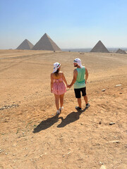 Couple walking hand in hand towards the Pyramids of Giza.