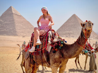Smiling woman on a camel with the pyramids of Giza in the background.