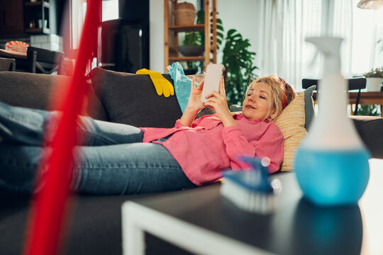 Housewife relaxing on sofa using smartphone after spring cleaning