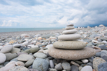 Zen stone balance on beach. Stacked pebbles on rocky beach. Zen stone tower balance on shore. Calm and serene coastal scene under cloudy sky