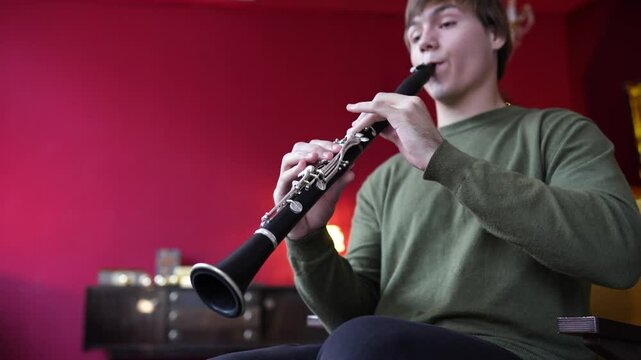 Clarinet player. Enthusiastic clarinetist playing flute woodwind music instrument sitting on armchair at home. Musical instruments. Man plays the oboe in living room. Relaxed mental hobby concept