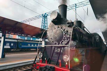 An old vintage steam locomotive is preparing to depart from the platform of a railway station. The historical era of steam engines. Traditional means of transportation in the 19th and 20th centuries