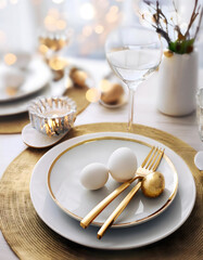 A minimalist Easter table setting with white eggs, gold cutlery, and a soft, blurred background