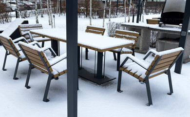 Snow-covered outdoor furniture in a backyard, with trees and hedges blanketed in snow