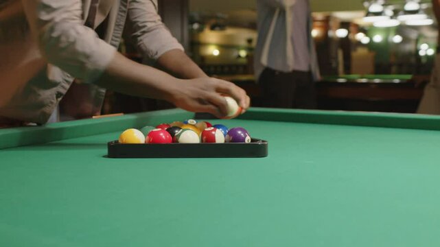 Midsection of anonymous man racking up colorful balls in triangle pyramid while preparing for pool game with friends in club