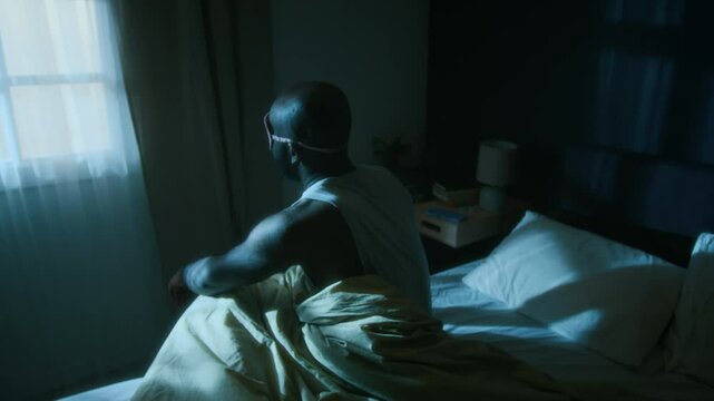 High angle shot of African American man, wearing pink sleep mask, standing up from his bed and sleepwalking at night