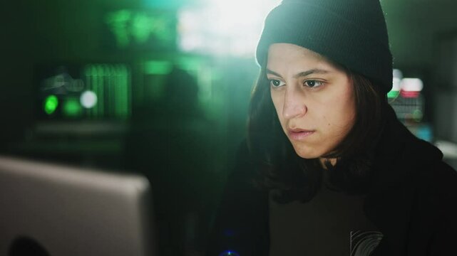 Female hacker breaking into a secure network, programming malicious code on her computer in a dark room