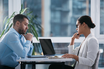 Two busy middle aged professionals man and woman business leaders partners checking document reading financial report talking working together on laptop computer in office at corporate meeting