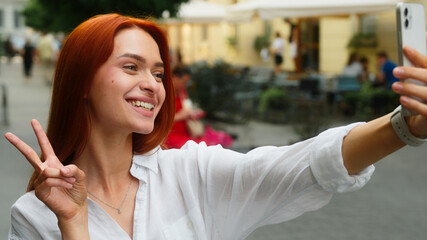 Happy smiling Caucasian woman girl tourist female student blogger vlogger influencer in city outdoors posing selfie photo sharing social media travel blog using mobile phone smartphone outside street