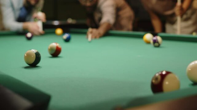 Closeup of anonymous man striking billiard ball and failing to sink it in hole while playing pool with friends indoors