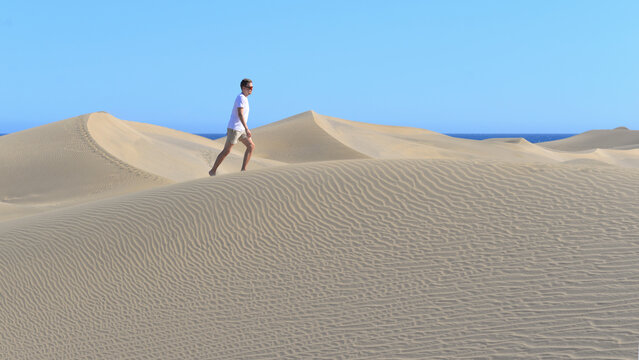 A man tourist in a dune at the sea background. A young man walking along desert barchans in Maspalomas, Gran Canaria. Touristic holiday vacation concept