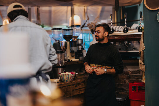 A barista standing behind a counter in a well-lit, cozy cafe with coffee equipment.