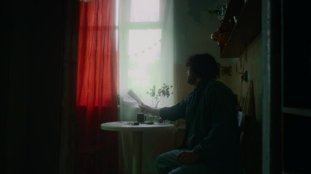 Full medium lowkey shot of disheveled-looking man feeling depressed after receiving past due bills, wandering round kitchen and taking seat in despair