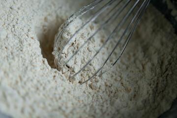 Whisking flour close up in mixing bowl with stainless steel whisk