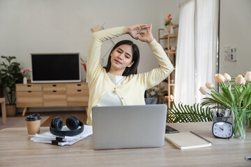 Young woman stretching at her desk in a home office, promoting wellness and relaxation during work.
