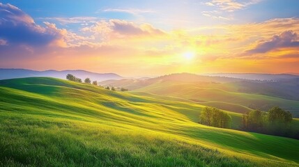 Obraz premium Vibrant sunset casts golden hues over rolling green hills in a serene landscape at dusk, capturing nature's tranquility and beauty