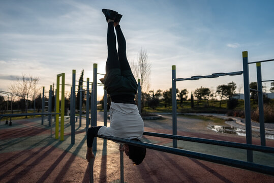 young athletic man exercising at fitness calisthenics workout and do handstand in parallel bars at street gym during sunset, body improvement and strength training concept