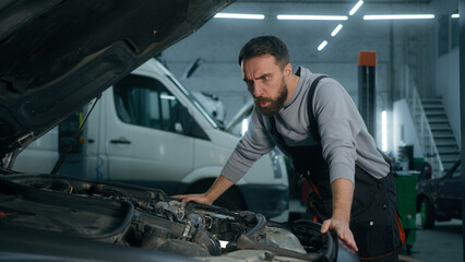 Confused shocked Caucasian guy man auto mechanic male repairman open hood bonnet fixing broken car at service station rubbing head automobile breakdown wreck crash transport vehicle repair in garage