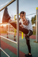 Obraz premium young athletic man exercising at fitness calisthenics workout and stretching legs at street gym during sunset, body improvement and strength training concept