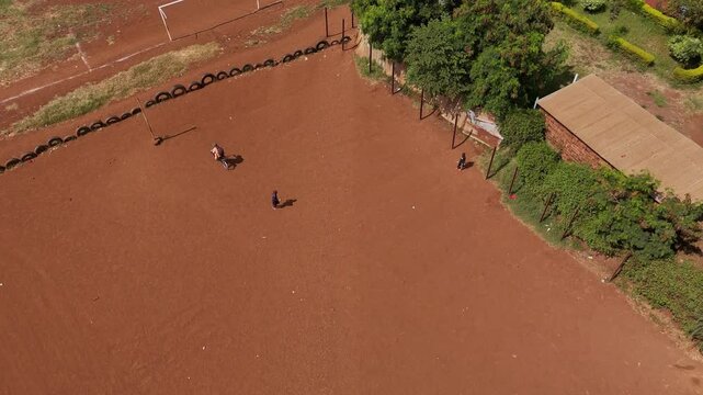 Aerial view of children playing on a dirt football field in Moshi