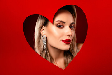 Lovely young woman with glamorous makeup in a heart frame on a red background, valentine day