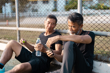 Senior men relaxing after exercise, enjoying water and conversation on a track.