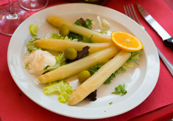 Baked white asparagus served with greens, olives, creamy mayonnaise and orange slice