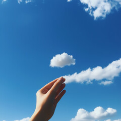A hand holds a small white cloud against a bright blue sky with scattered clouds.