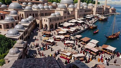 Aerial video captures a bustling waterfront market with traditional architecture, vibrant stalls, and boats, showcasing a lively, historical atmosphere.