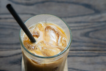 A close-up of an iced latte served in a glass with ice cubes and a straw, placed on a wooden table, highlighting its refreshing and creamy texture