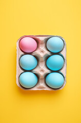 A square package of pastel eggs, set against a yellow background.Minimal creative Easter holiday food advertise concept.Copy space,flat lay 