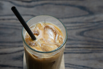 A close-up of an iced latte served in a glass with ice cubes and a straw, placed on a wooden table, highlighting its refreshing and creamy texture