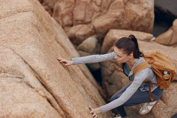 A determined young woman climbing a rocky surface during outdoor adventure, showcasing strength,...