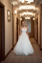 Beautiful blonde bride in a long white dress walks along the hotel corridor