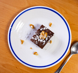 Small piece of brawny with nuts dished up in service plate with dessert spoon