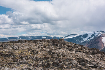 Sunlit big rocky hill of sharp stones against mountain range silhouette and snow mountains in...