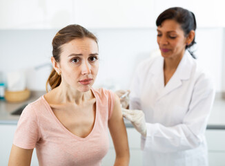 Portrait of scared young adult woman getting injection during visit at doctors office