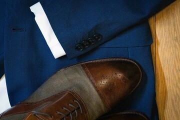A pair of shoes and a jacket are displayed on a wooden surface. The shoes are brown and the jacket is blue. Concept of sophistication and elegance, as the combination of the shoes