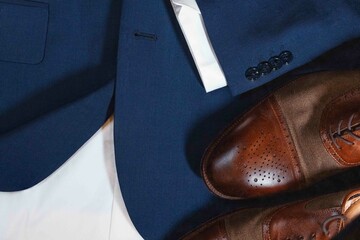 A pair of brown shoes with a white stripe on the side sit on a blue jacket. The jacket is a dark blue color and has a white collar