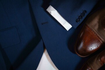A pair of brown shoes and a blue suit jacket are displayed on a table. The jacket is made of a blue fabric and has a white collar. The shoes are brown and have a pointed toe